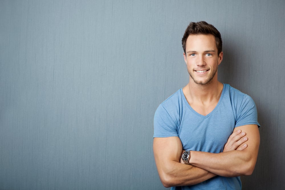 Smiling young man standing with arms crossed against gray background