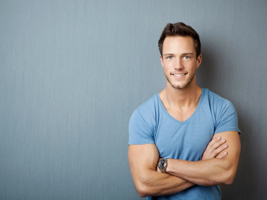 Smiling young man standing with arms crossed against gray background1